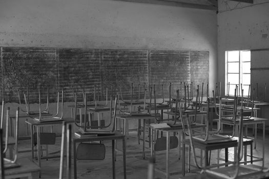 Grayscale image of an empty classroom in Bulawayo, Zimbabwe, with desks and chairs arranged neatly.
